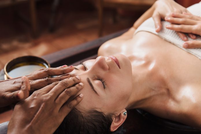 Ayurvedic face massage with oil on the wooden table