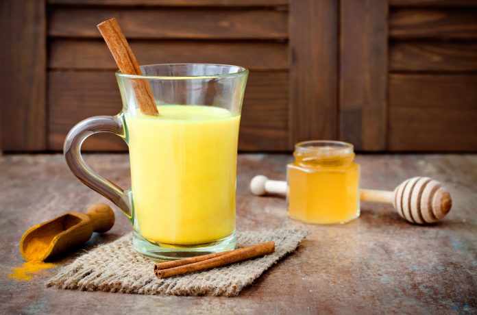Turmeric golden milk latte with cinnamon sticks and honey. Detox liver fat burner, immune boosting, anti inflammatory healthy cozy drink