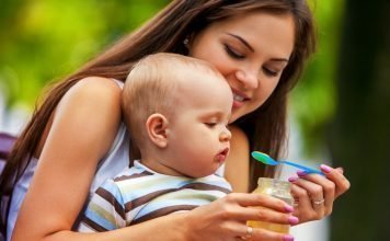 Baby feeding spoon by mother in park outdoor. Weaning .