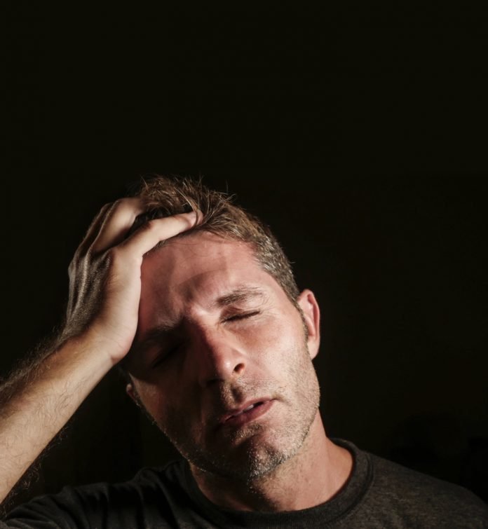 young attractive and sad man suffering depression and headache with hand on his tempo head in stress looking worried and sick isolated on black