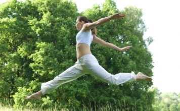 Sporty girl exercising on meadow against the sky.