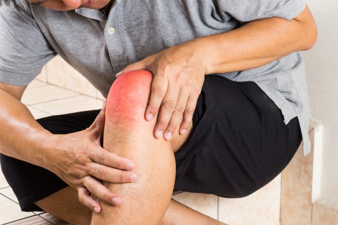 Matured man suffering from painful knee joint seated on steps