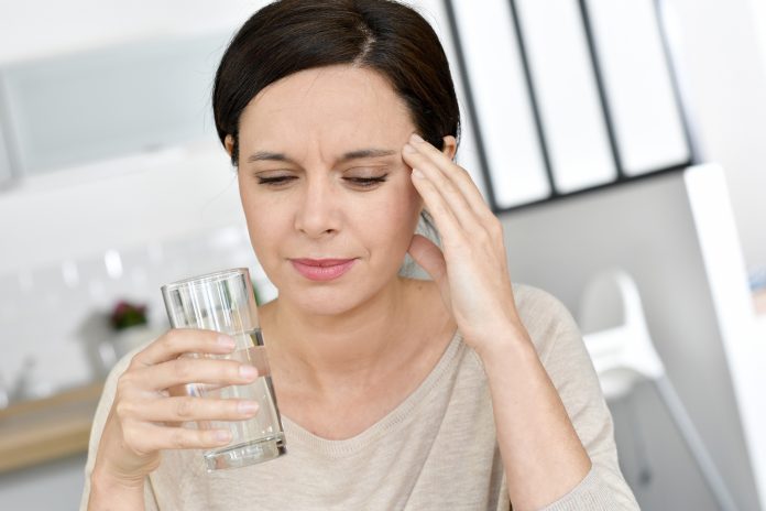 Mature woman having migraine, drinking water