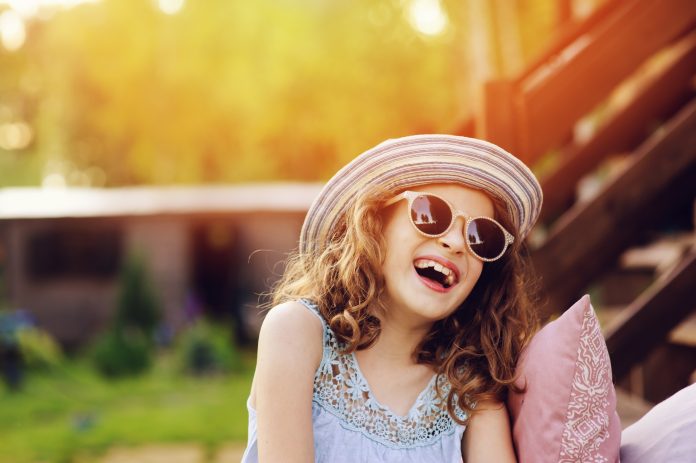 summer portrait of happy kid girl on vacation in sunglasses and hat, laugh and showing tongue.