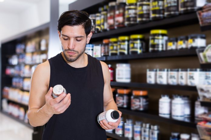 Serious young muscular man choosing sport dietary supplements