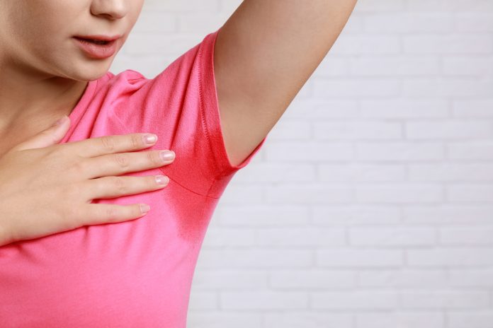 Young woman with sweat stain on her clothes against brick wall, closeup. Using deodorant
