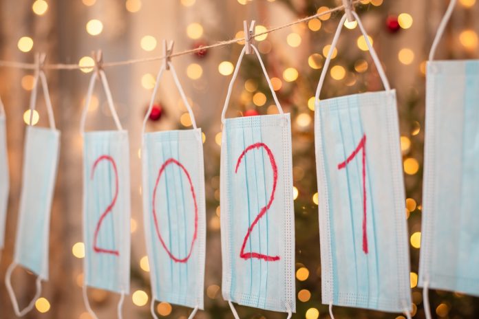 Garland made of medical masks on the background of decorated christmas tree with many bright lights. Celebrating new 2021 year during the pandemic
