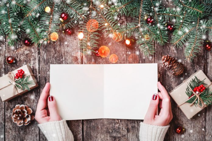 Female hand reading a letter to Santa on wooden background with Christmas gifts, Fir branches. Xmas and Happy New Year. top view