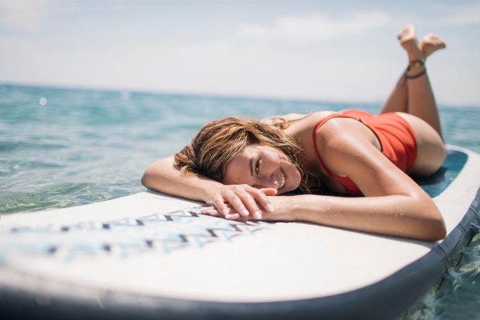 Smiling woman enjoys sunbathing on paddle board