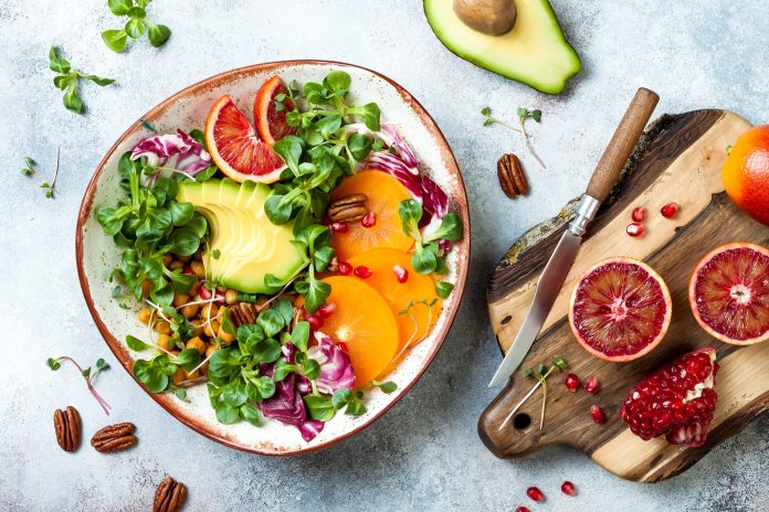 Vegan, detox Buddha bowl with turmeric roasted chickpeas, greens, avocado, persimmon, blood orange, nuts and pomegranate. Top view, flat lay