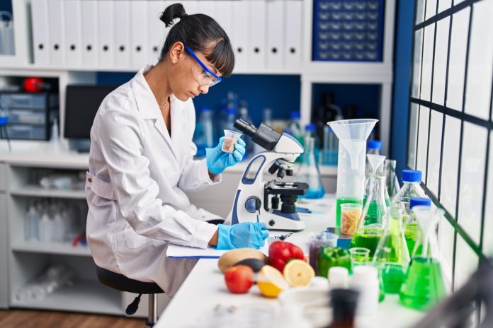 Young beautiful hispanic woman scientist writing on document at laboratory