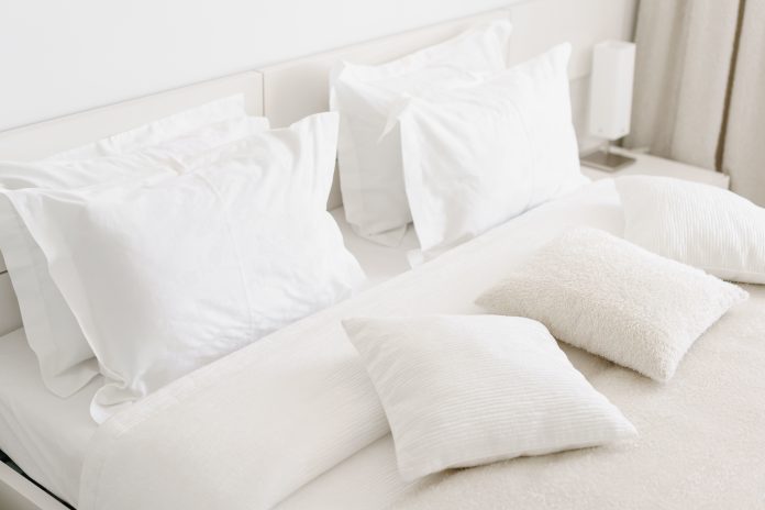 Comfortable soft pillows on the bed. Close-up white bedding sheets and pillow on light wall room background. Fresh bed concept